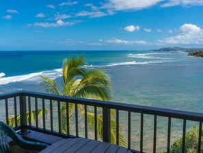 A balcony with a view of the ocean, palm trees, and a distant landmass. - Sealodge-Condo-D6 (Princeville)