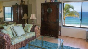 Ein Wohnzimmer mit einer Couch, einem Glastisch, einem Holzschrank und einem großen Fenster mit Blick auf den Ozean.