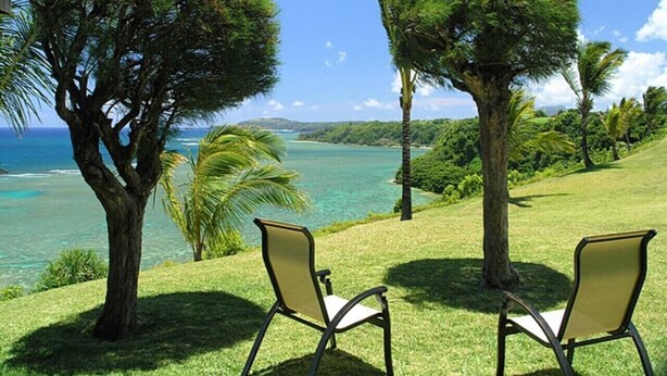 Une zone herbeuse avec deux chaises et des arbres, donnant sur une étendue d’eau.