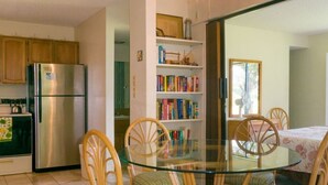Une cuisine équipée d’un réfrigérateur, de meubles de rangement en bois, d’une table à manger en verre avec des chaises et d’une bibliothèque.