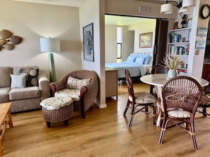 A living room with a sofa, two wicker chairs, a round table, and a bookshelf.