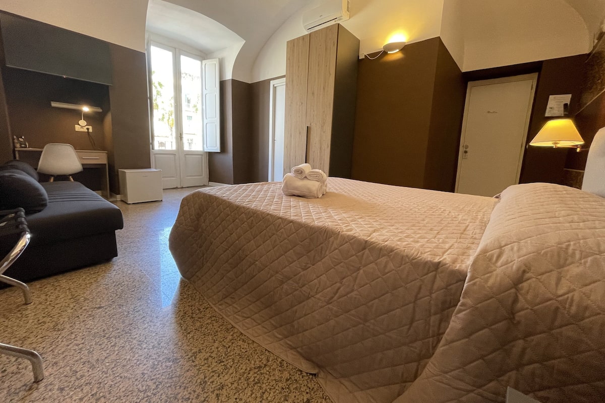 Habitación de hotel con una cama grande, un escritorio, una silla y una ventana con cortinas.