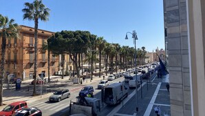 Una concurrida calle urbana con palmeras, coches estacionados y un edificio histórico con balcones.