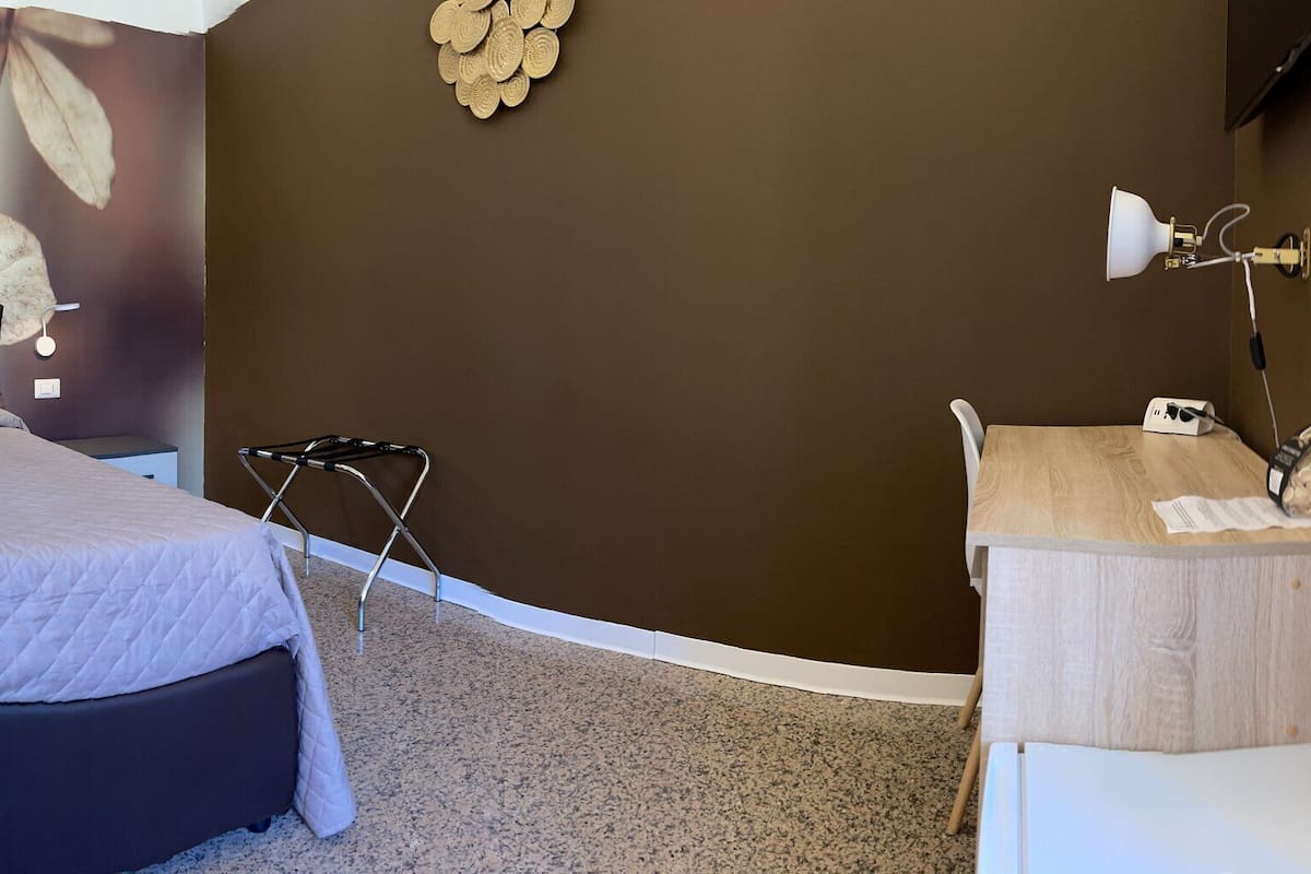 Un dormitorio con cama, mesita de noche, espejo, toalla y una pared con diseño floral.