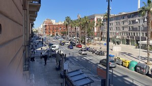 Una concurrida calle urbana con edificios, palmeras y coches aparcados.