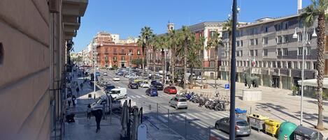 A busy urban street with buildings, palm trees, and parked cars.
