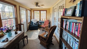 A cozy reading nook with a bookshelf, two chairs, a desk, and a ceiling fan.