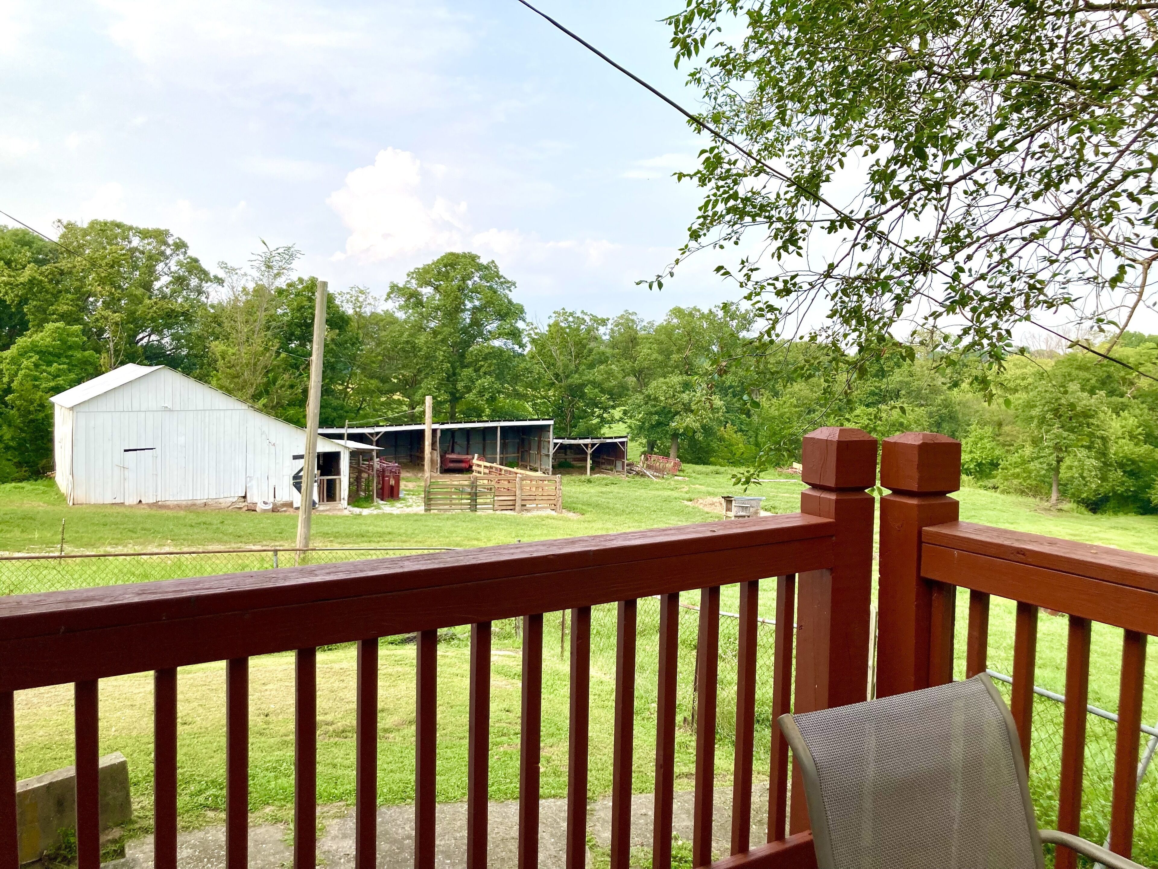 A wooden deck with a metal chair, overlooking a rural landscape with a barn and open fields.
