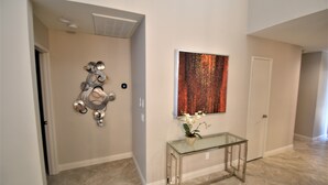 A hallway with a glass console table, a decorative wall piece, and a door. - Palm Valley CC Remodeled beauty, 2b 2ba on 6th fairway w/golf cart, club access. (Palm Desert)
