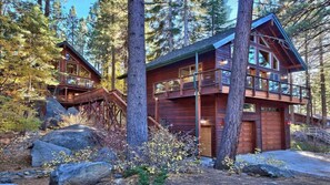 A cabin with a wooden exterior, built on stilts, surrounded by trees and rocks.