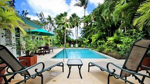 Area piscina con lettini e un tavolo, circondata da lussureggiante vegetazione tropicale.