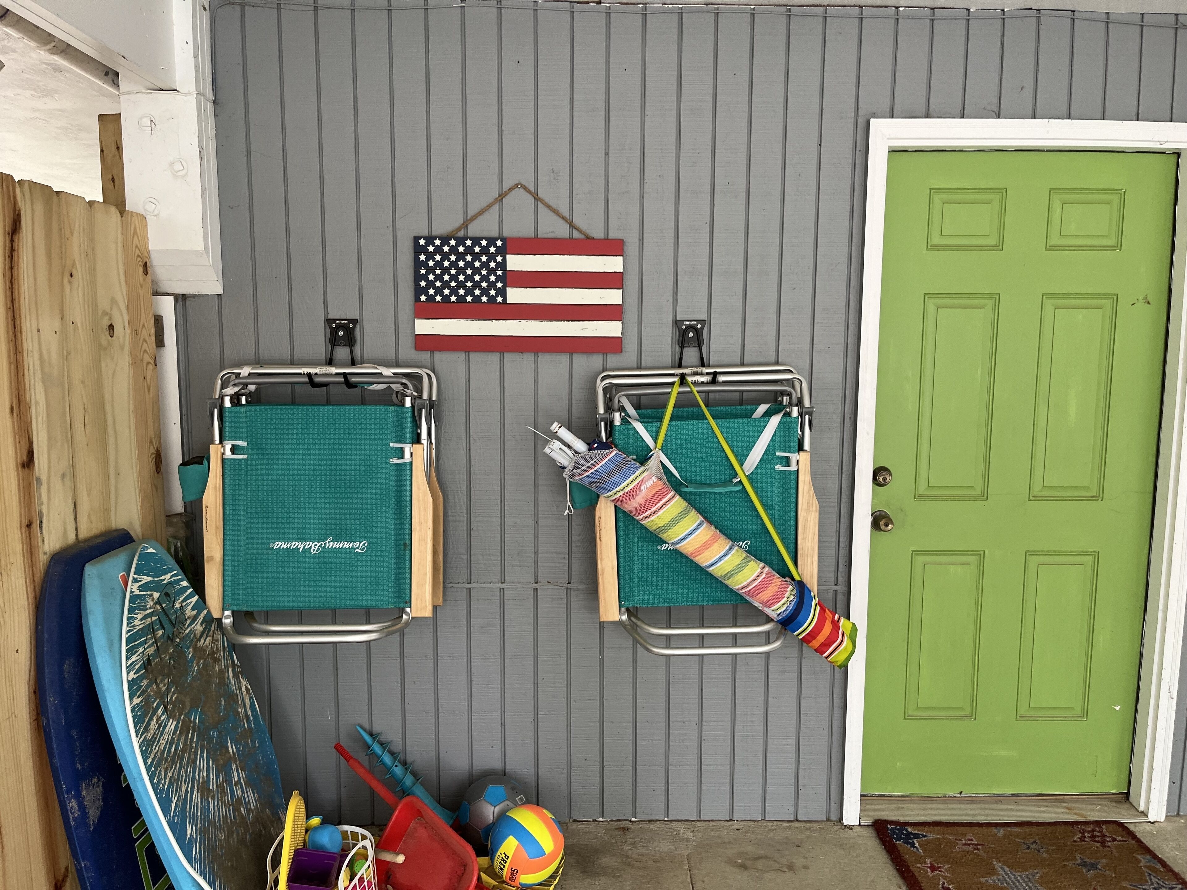 Une pièce avec deux chaises pliantes vertes, une serviette rayée aux couleurs vives, une planche de surf bleue et un ballon de volley-ball.