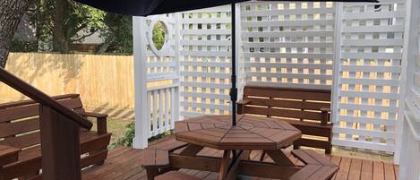 Um deck de madeira com mesa de piquenique e bancos, cercado por uma vedação de treliça branca.