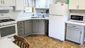 A compact kitchen with white cabinets, a stove, a refrigerator, and a microwave. - Backroad Pines Hideaway
Your ATV & Waterfall Adventure Basecamp! (Dunbar)