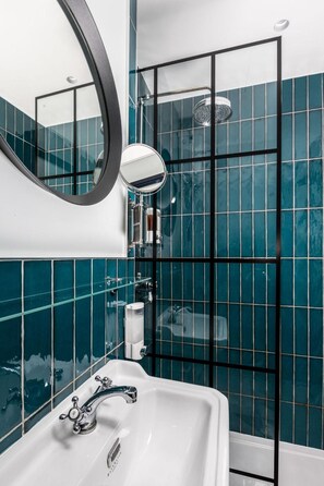 A bathroom with a white sink, a round mirror, and a shower enclosure with a glass door. - The Camden Town Hotel (London)