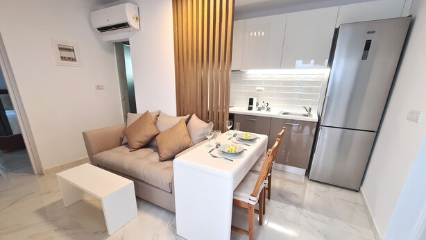 A modern living room with a sofa, coffee table, and dining table set for two. A kitchen with a refrigerator and cabinets is visible in the background. - Deluxe house, 5 min. walk from Old Town, Acropolis and city centre. Free Wi-Fi. (Ρόδος)