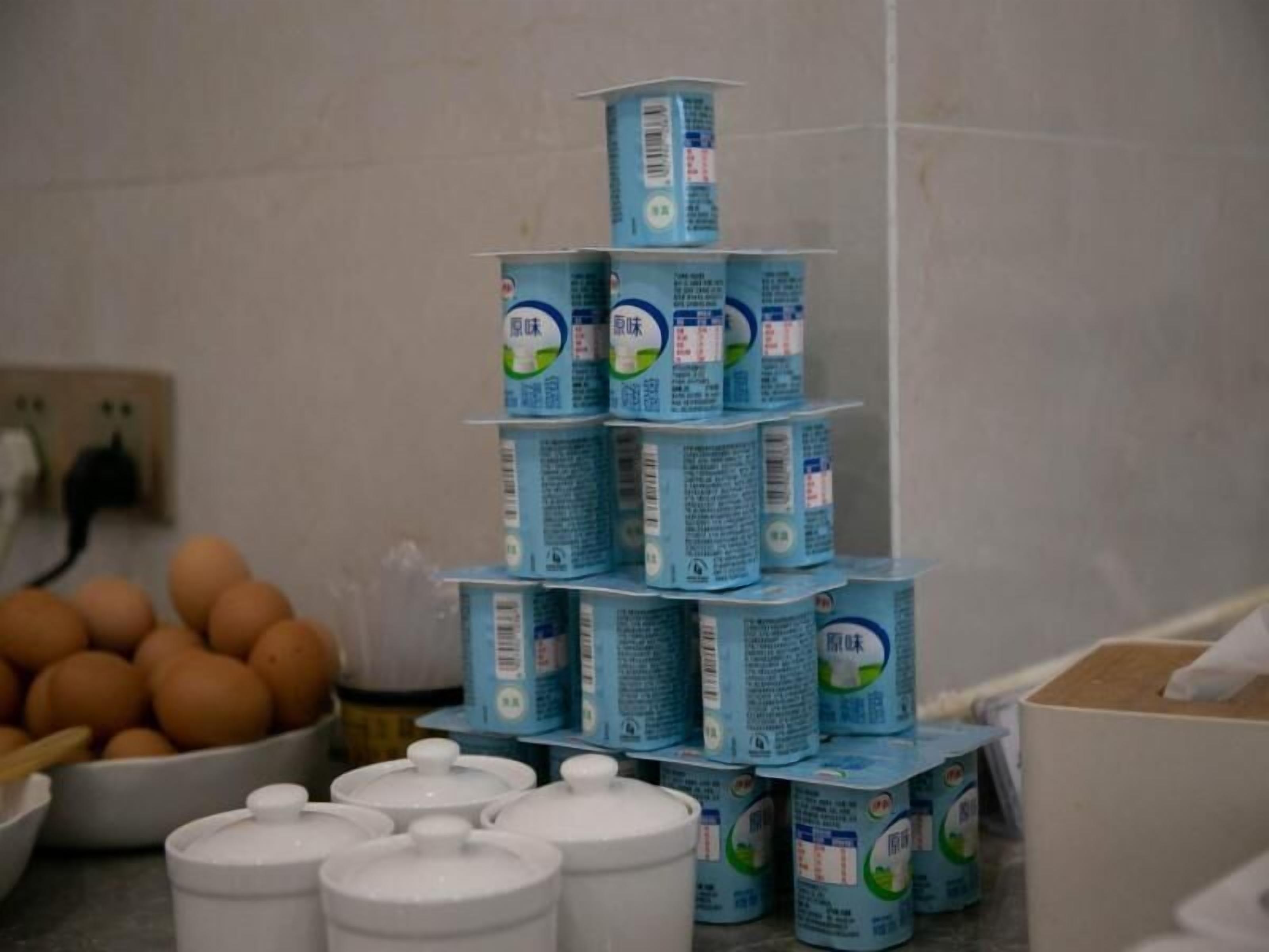 A kitchen with a stack of blue milk cartons, a bowl of eggs, and white containers on the counter.
