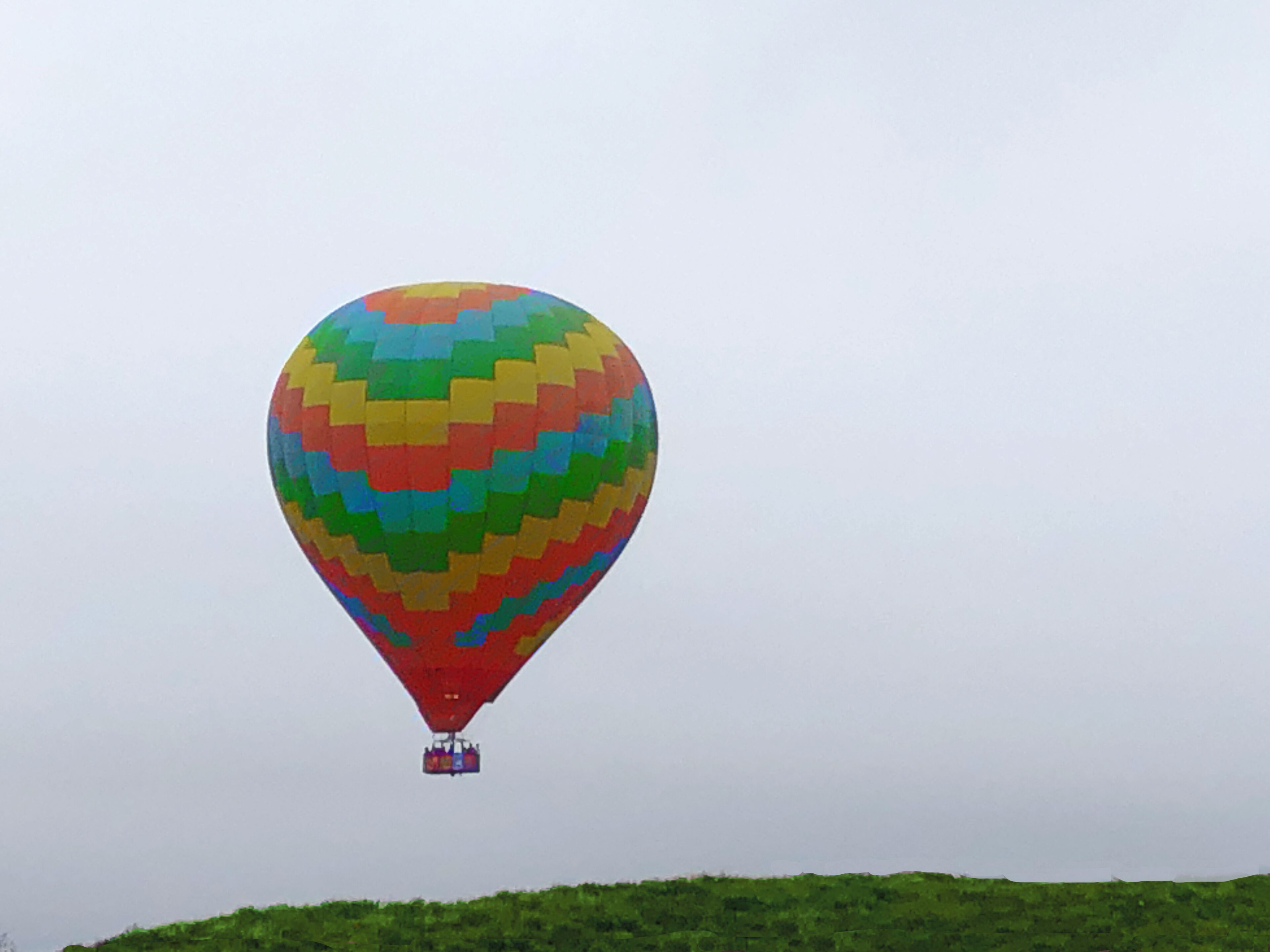 A hot air balloon with a colorful pattern, flying over a green landscape.