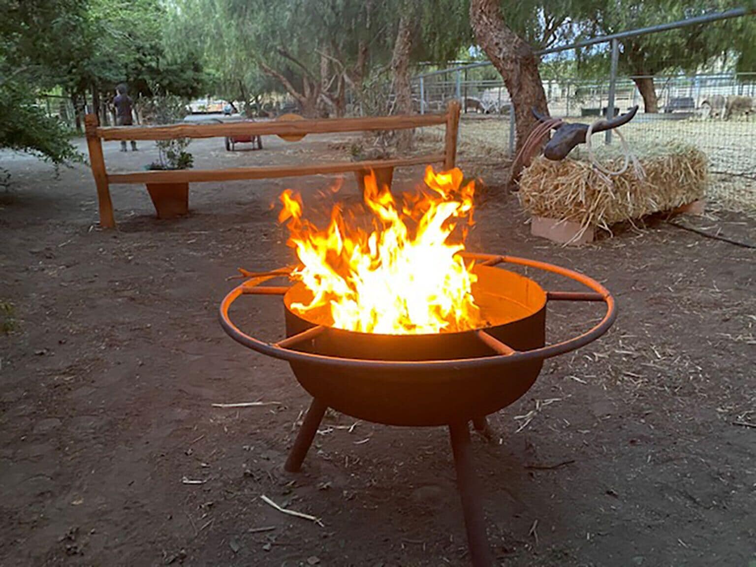 Un fuoco di campo in un braciere metallico, con una panca e balle di fieno sullo sfondo.
