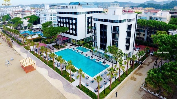 Et moderne hotel med en stor swimmingpool omgivet af palmer og udendørs siddepladser.