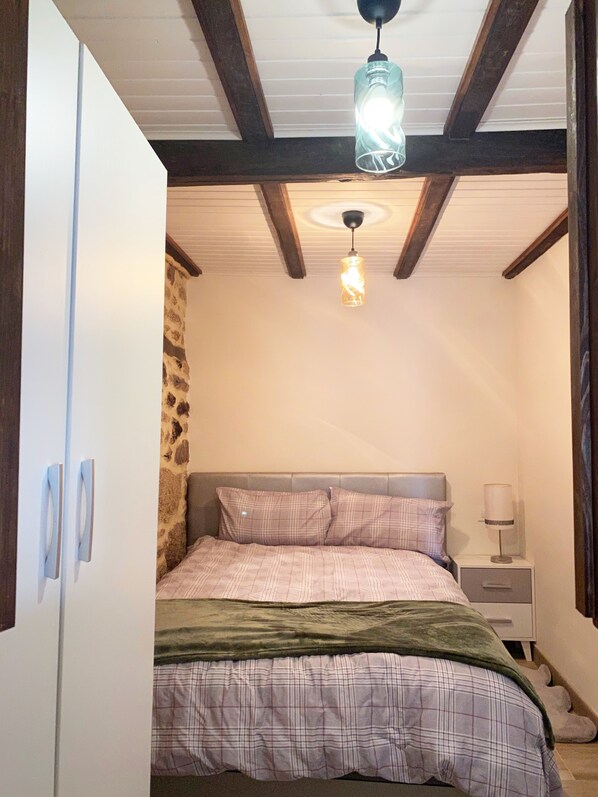 A bedroom with a bed, a nightstand, a lamp, a wardrobe, and a hanging light fixture.