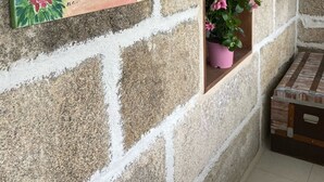 En stenmur med en färgstark målning som föreställer ett kustlandskap, en krukväxt och en trälåda.