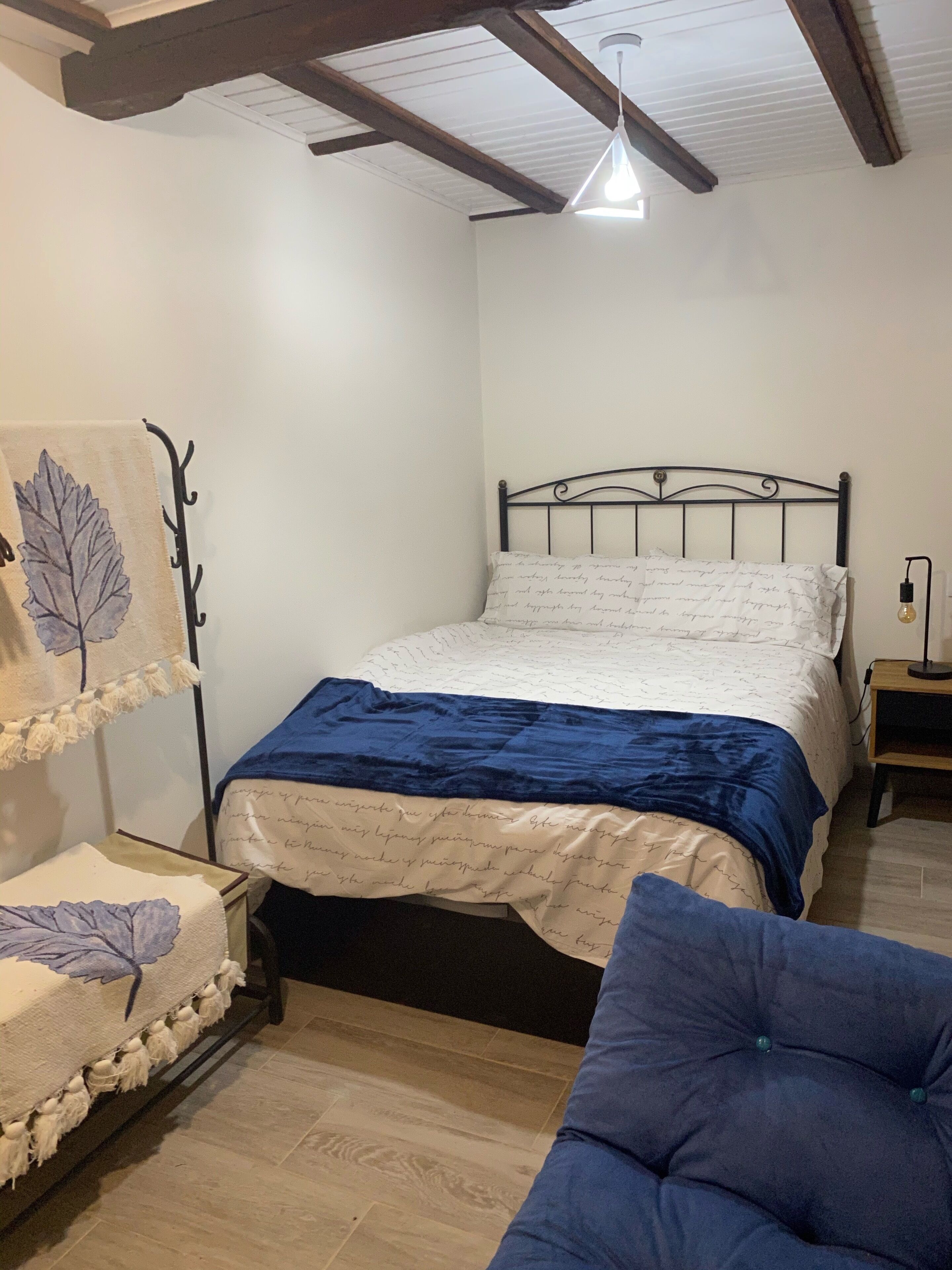 Quarto com cama, mesa de cabeceira, luminária pendente e prateleira na parede.