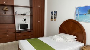 A bedroom with a bed, a wardrobe, a desk with a computer, and a painting of a beach scene.