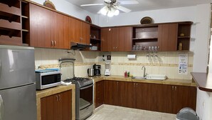 A kitchen with wooden cabinets, a stainless steel refrigerator, a microwave, a stove, and a ceiling fan.