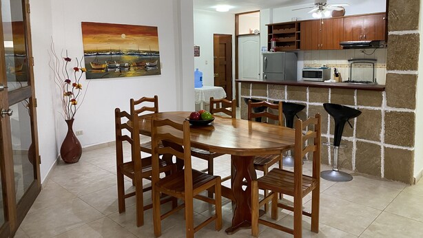 A dining area with a wooden table and chairs, a vase with flowers, and a painting on the wall.