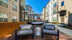 Eine Terrasse im Freien mit zwei grauen Sofas und einem weißen Tisch, umgeben von Holzboden und einer Holzwand.