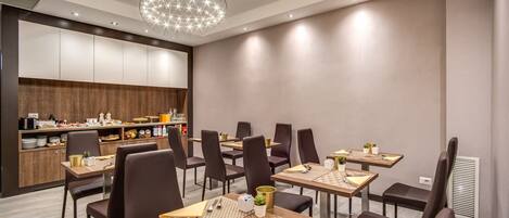 A modern dining area with multiple tables and chairs, a kitchen in the background, and a decorative ceiling light.