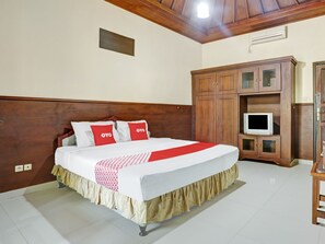Una cama bien hecha con una colcha blanca y roja, un cabecero de madera y un televisor sobre un mueble de madera.