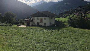 A white building with a dark roof, surrounded by green fields and mountains. - A wonderful panoramic apartment of 110m2. (Radenthein)
