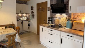 Une cuisine compacte avec des meubles blancs, un pare-feu en pierre et une hotte noire.