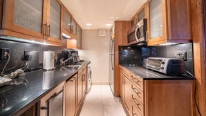 A modern kitchen with wooden cabinets, a black countertop, a built-in oven, a microwave, and a toaster. - Cozy Quaint Condo steps away from Vail Village  and  Gondola, Hot tub + Sauna access (Vail)