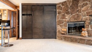 A modern interior with a dark wooden wardrobe, a stone fireplace, and a bar area with stools. - Cozy Quaint Condo steps away from Vail Village  and  Gondola, Hot tub + Sauna access (Vail)