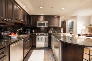 A modern kitchen with dark wood cabinets, stainless steel appliances, and a granite countertop. - Charming Corner Condo, fireplace, spa access, two steps to Vail Village  and  Lifts (Vail)