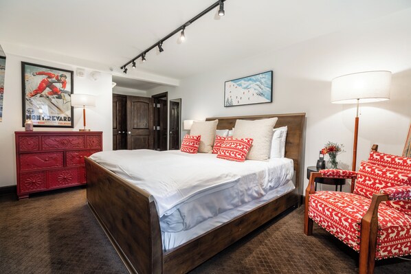 A bedroom with a wooden bed, red patterned chairs, a red dresser, and a framed poster on the wall.
