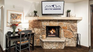 Una chimenea de piedra con un televisor encima, un escritorio con una silla, y un cuadro en la pared.