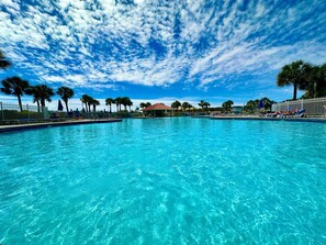 A clear blue pool with a view of palm trees and a building in the background.