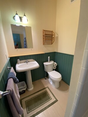 Ein Badezimmer mit einem Waschbecken auf Säule, Toilette und einem Spiegel darüber.