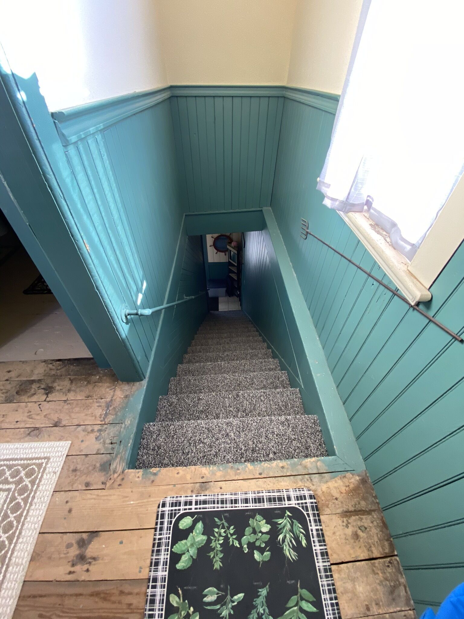 Een trap met turquoise wanden en een houten vloer, die leidt naar een kamer met een raam en een deur.