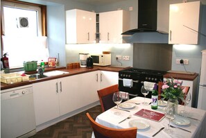 Une cuisine compacte avec des meubles blancs, une cuisinière noire et une table à manger pour deux personnes, agrémentée de verres à vin et d’un menu.