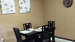 Un coin repas avec une table et des chaises, une horloge au mur et deux tableaux représentant des motifs floraux.