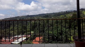 Un balcon offrant une vue sur un paysage vallonné, avec des maisons et de la verdure.