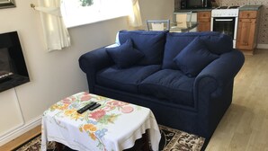 Een woonkamer met een donkerblauwe bank, een bloemen tafelkleed en een afstandsbediening op een bijzettafeltje.