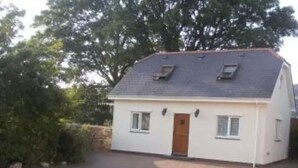 Een gelijkvloers huis met schuin dak, een centrale deur en twee ramen aan de voorgevel.