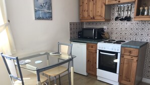 Een compacte keuken met een glazen eettafel, houten keukenkastjes, een magnetron en een kookplaat.