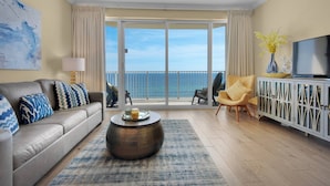 A modern living room with a sofa, armchair, and coffee table, a television, and a view of the ocean through large sliding doors. - Boardwalk Beach Resort Unit 905 (Panama City Beach)
